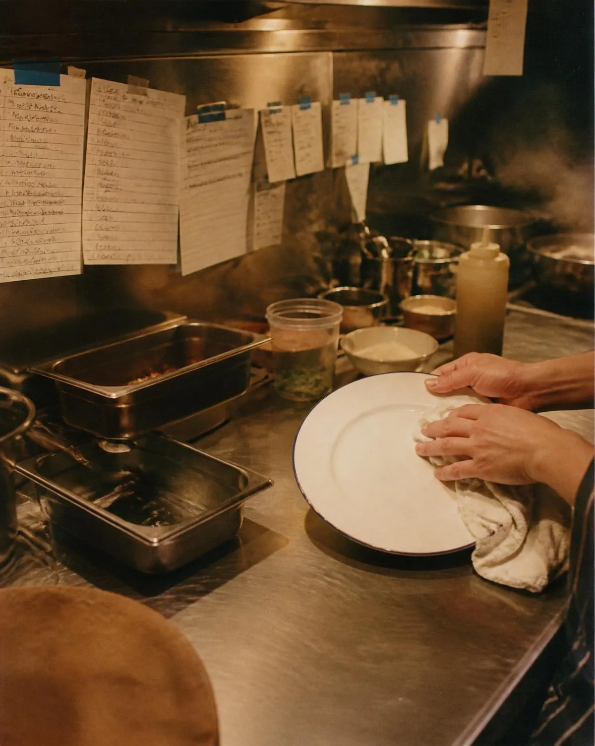 Hands polishing a plate on a kitchen bench before service